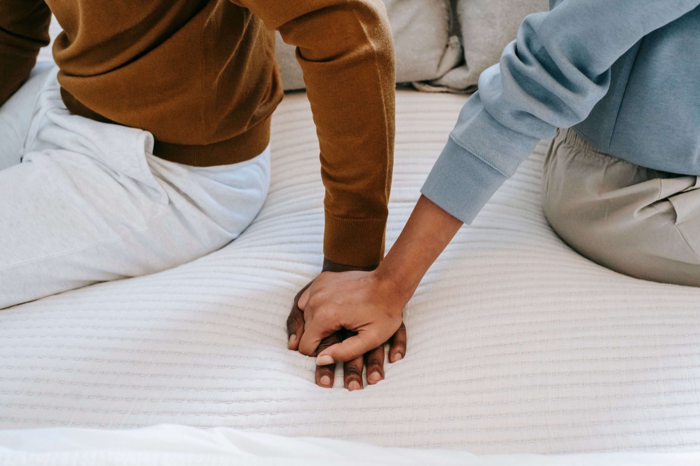 Two people sitting on a bed, one gently holding the other’s hand