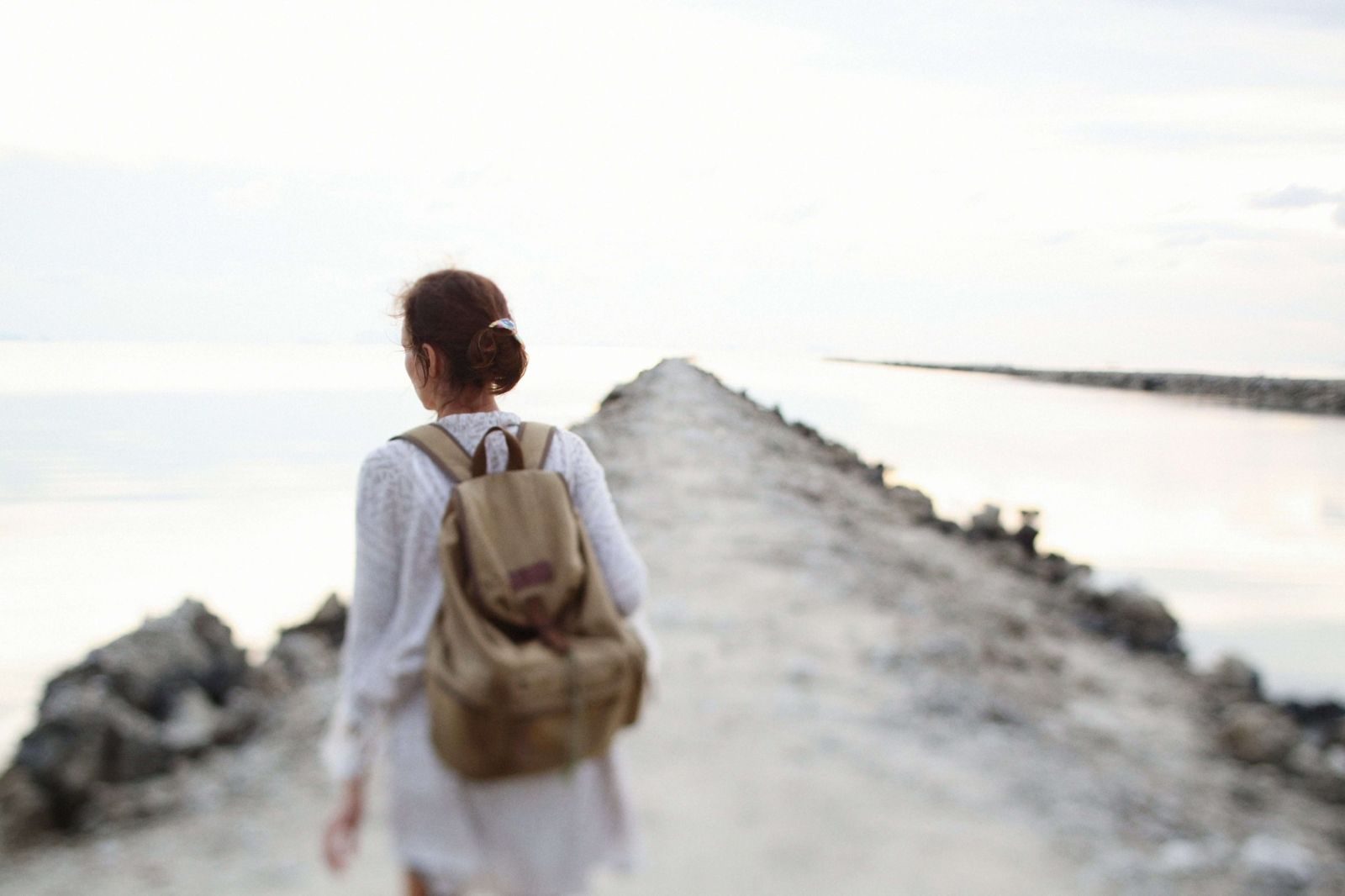 A woman walking alone along a stone path by the sea